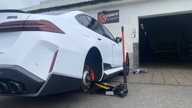 White BMW M5 outside the workshop with its rear wheel removed.
