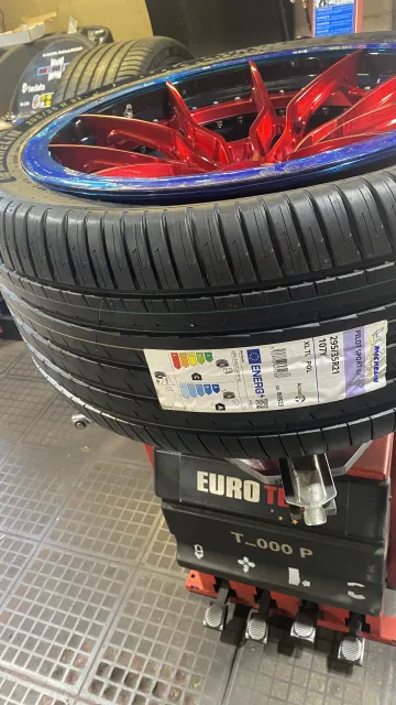 New Michelin tyre on a red-spoked wheel with a blue rim on the tyre fitting machine.