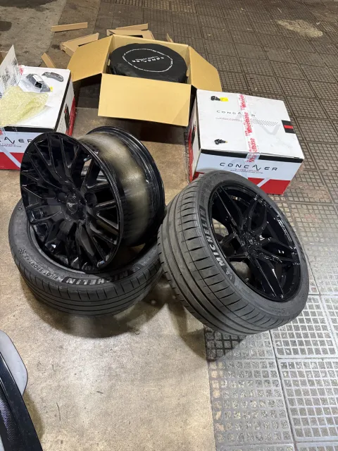 Black alloy wheels and Michelin tyres beside wheel packaging on the workshop floor.