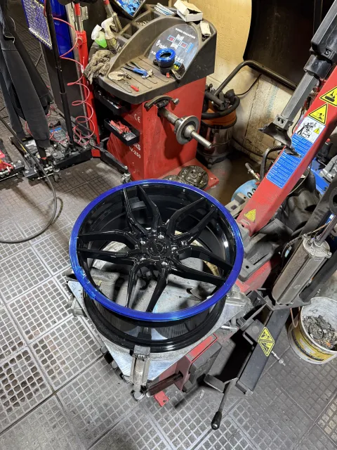 Black multi-spoke alloy wheel on the tyre-fitting machine with a blue rim protector.